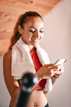 Beautiful young woman using smarthphone while exercising on stepper at home.