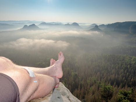 Hiker and hiker with bare feet lie on the edge of a rock massif and relax. View over crossed legs of a resting male body into a wooded landscape