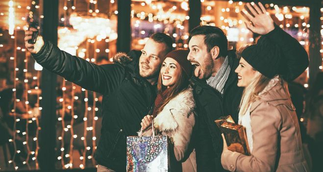 Young beautiful cheerful friends taking a selfie in the city street at new year's night with a lot of lights on background. 