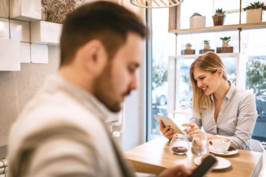 Young smiling businesspeople surfing the internet on a break in a cafe. Smiling woman using digital tablet and drinking coffee. Man using smarthphone.