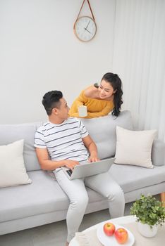 Cheerful young beautiful couple chatting with laptop and coffee at home.