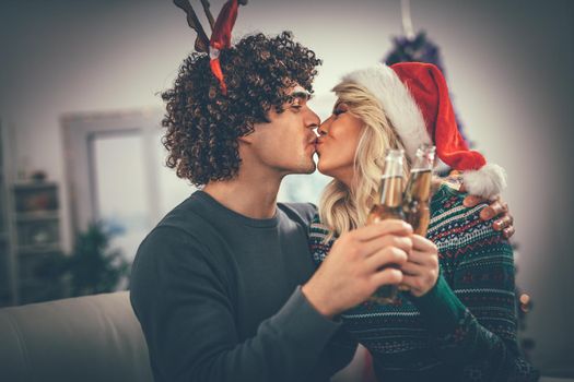 Young romantic couple hugging and kissing in Christmas time. They are toasting with bottles of drink.