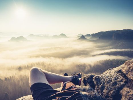Resting man. Traveler\'s naked legs pointed towards to mountain peaks at distance over foggy clouds