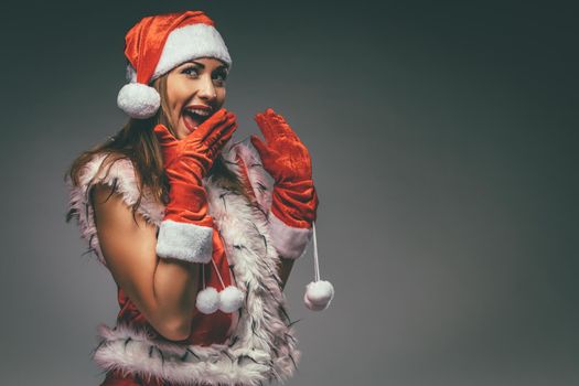 Portrait of a beautiful young smiling woman in Santa Claus costume having fun and surprised looking at camera.