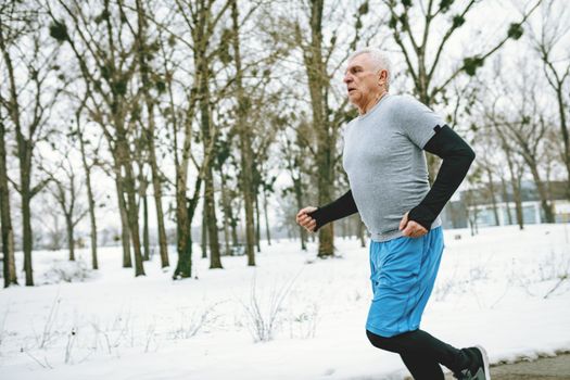 Active senior man running and doing exercises in public park during the winter training outside in. Copy space. 