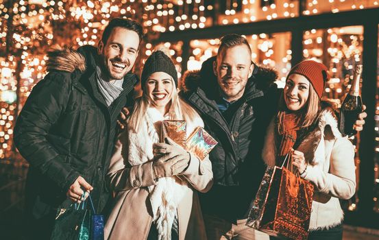 Group of four happy young friends enjoying in Christmas night shopping with bright shop window in background.