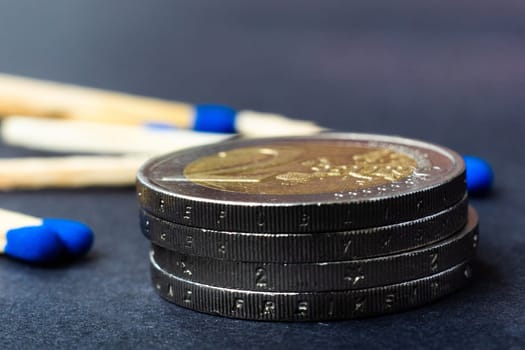 Blue matches and stack of coins on a dark background macro