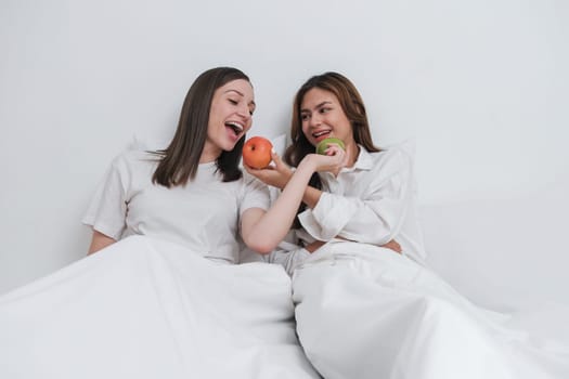 Asian cheerful happy young lesbian caucasian couple resting and eat fruit on bed at home. Concept of homosexual relationship. Morning timetogether on bed in bedroom.