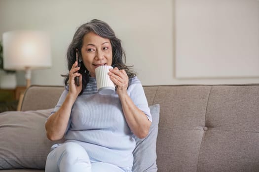 A happy 60s Asian woman enjoys her coffee and talking on the phone.