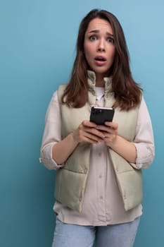 upset brunette young woman holding a smartphone in her hands on a studio background.