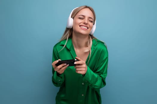 photo of a cute cheerful attractive blonde young woman in headphones with a smartphone in her hands on a blue background.