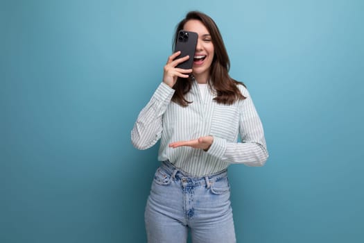 cute young brunette woman in a shirt makes a photo on a smartphone on a studio background.