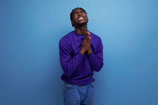 praying black american young brunette man with dreadlocks in a blue hoodie.