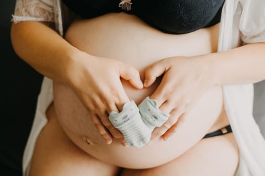 Young pregnant woman with baby socks on a belly, pregnancy concept