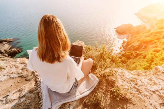 Freelance woman working on a laptop by the sea, typing away on the keyboard while enjoying the beautiful view, highlighting the idea of remote work