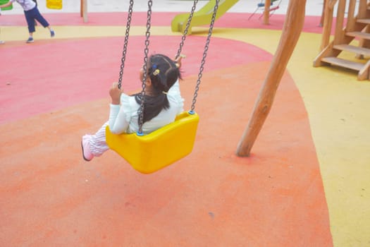 child having fun on a swing on the playground in public park