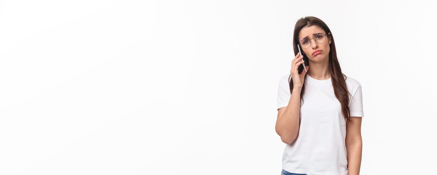 Communication, technology and lifestyle concept. Portrait of gloomy and sad young woman calling someone and left hanging on phone waiting for answer, pouting and frowning uneasy, white background.