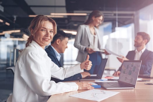 businesswoman sitting at the office table with group of colleagues, working on laptop.