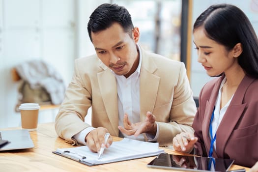 Businessman manager explaining and coaching Asian colleague financial project on paperwork.