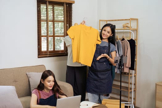 Beautiful asian woman showing clothes for sale in front of camera for live streaming at home.