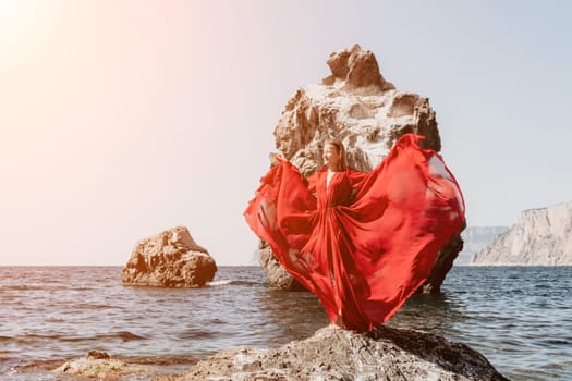 Woman travel sea. Young Happy woman in a long red dress posing on a beach near the sea on background of volcanic rocks, like in Iceland, sharing travel adventure journey