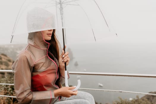 Woman rain park. Happy woman portrait wearing a raincoat with transparent umbrella outdoors on rainy day in park near sea. Girl on the nature on rainy overcast day