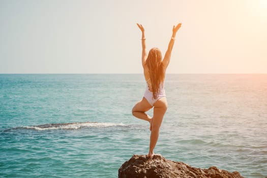 Woman sea yoga. Back view of free calm happy satisfied woman with long hair standing on top rock with yoga position against of sky by the sea. Healthy lifestyle outdoors in nature, fitness concept