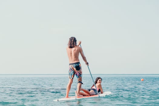Silhouette of woman standing, surfing on SUP board, confident paddling through water surface. Idyllic sunset or sunrise. Sports active lifestyle at sea or river.