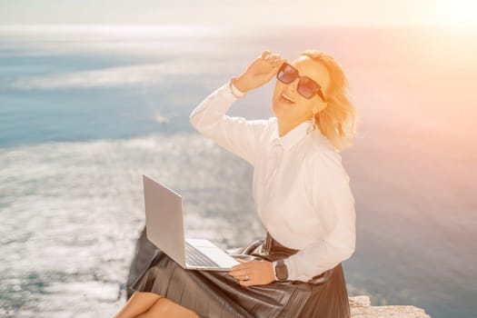 Business woman on nature in white shirt and black skirt. She works with an iPad in the open air with a beautiful view of the sea. The concept of remote work