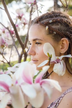 Magnolia flowers. Happy woman enjoys by blooming magnolia tree and sniffs it flowers with closed eyes in spring garden. Portrait