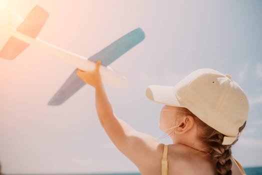 Kid playing with toy airplane. Children dream of travel by plane. Happy child girl has fun in summer vacation by sea and mountains. Outdoors activities at background of blue sky. Lifestyle moment