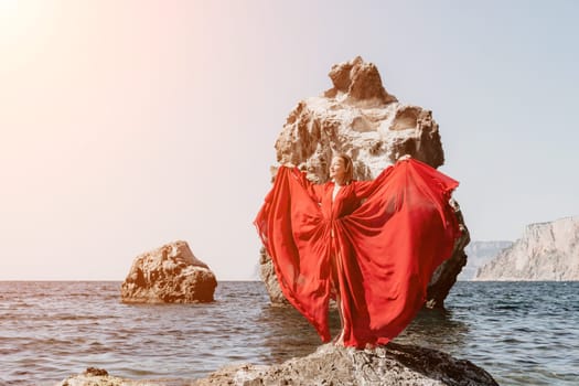 Woman travel sea. Young Happy woman in a long red dress posing on a beach near the sea on background of volcanic rocks, like in Iceland, sharing travel adventure journey