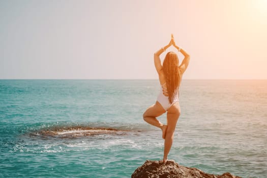 Woman sea yoga. Back view of free calm happy satisfied woman with long hair standing on top rock with yoga position against of sky by the sea. Healthy lifestyle outdoors in nature, fitness concept