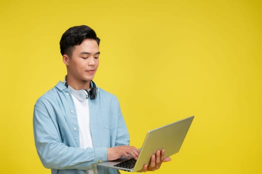 Smiling young man using laptop and looking at camera over yellow background
