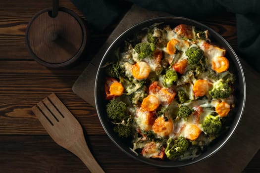 Gratin with broccoli, carrots and cheese baked in the oven on a dark wooden table.
