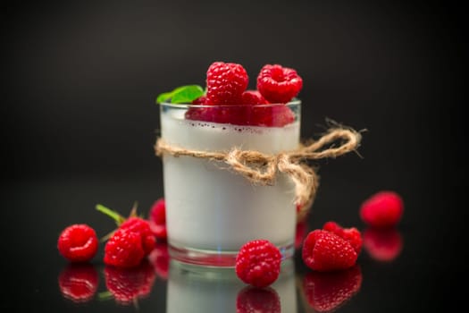 Cooked homemade yogurt with ripe red raspberries in a glass isolated on a black background