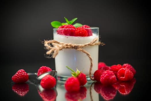 Cooked homemade yogurt with ripe red raspberries in a glass isolated on a black background