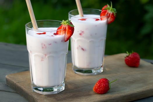 Strawberry smoothie in two glass glasses and fresh strawberries on a wooden table in the yard.