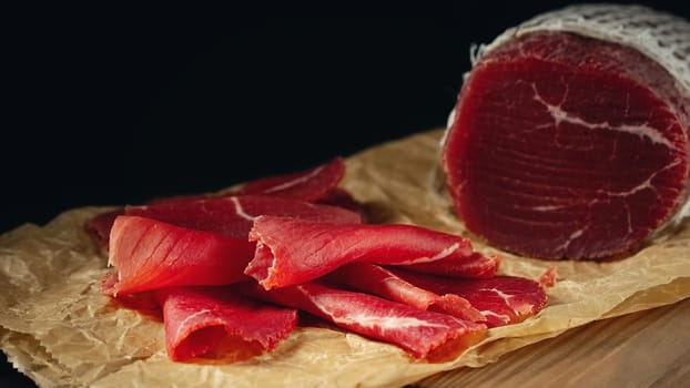 Whole and sliced bresaola on paper on a cutting board.