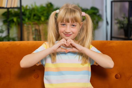 I love you. Child kid girl makes symbol of love, showing heart sign to camera, express romantic feelings, express sincere positive feelings. Charity, gratitude, donation. Female teen toddler at home