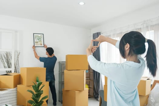 Man hanging picture on white wall in room. Happy Couple Hanging Picture on the Wall, Boyfriend Moves It, Girlfriend Tells Him when the Frame is Hanging Straight. Moving to new house, new ownership and real estate concept.