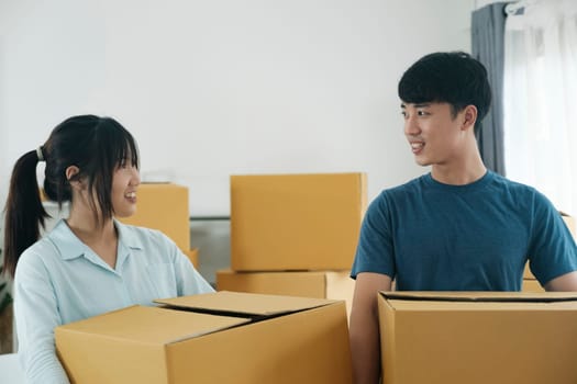 Asian young happy new married couple moving to their new house or real estate. An attractive romantic man and woman carry boxes parcel with happiness and love. Family moving house relocation concept.