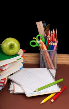 board, books, pencils, opened empty notebook against a dark background