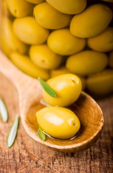 Close up green olives in bank, rosemary on a wooden background