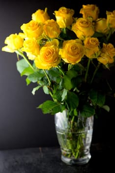 bouquet of beautiful yellow roses with leaves in a vintage crystal vase on a black