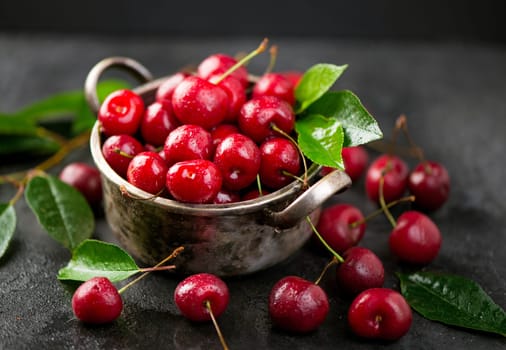 Cherry summer background. A large number of cherries with leaves on the table in a saucepan on a black background.