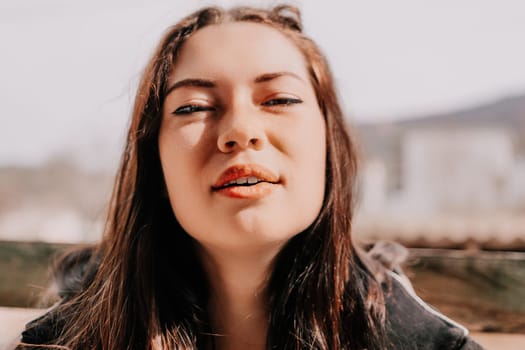 Happy young smiling woman with freckles outdoors portrait. Soft sunny colors. Outdoor close-up portrait of a young brunette woman and looking to the camera, posing against nature background.