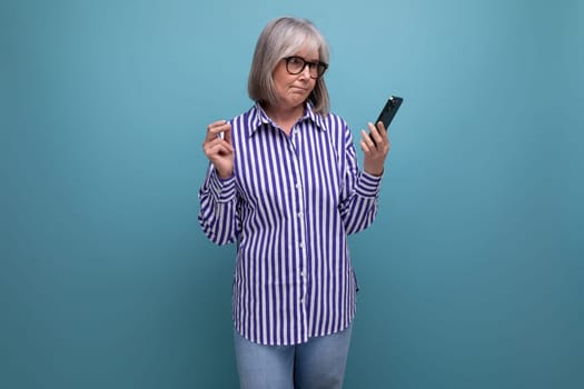 modern 50s middle aged woman with gray hair in trendy outfit mastering smartphone on bright studio background with copyspace.