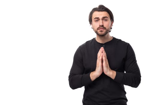 young handsome brunet european man in a black sweater folded his hands on an isolated white background.