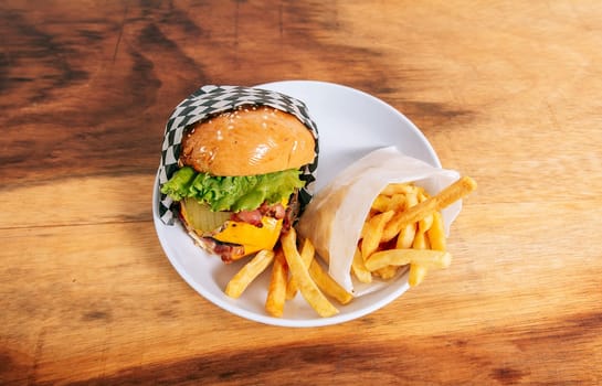 Big cheeseburger with french fries served on wooden table. Delicious homemade hamburger on a plate on a wooden table